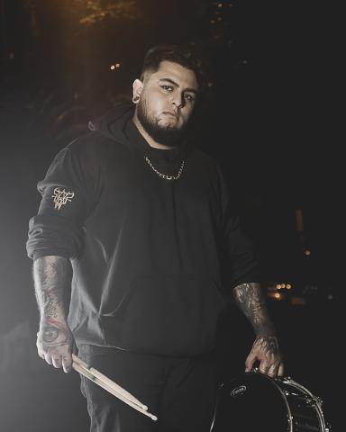 Foto de baterista de la banda ground of chaos sostienendo un redoblante y unas baquetas en la noche con ropa negra